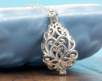 May include: A silver-toned metal pendant necklace featuring an intricate, openwork filigree design shaped like a teardrop. The pendant is suspended from a delicate silver-colored chain, showcasing detailed swirling patterns and a central floral motif.