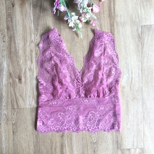 May include: A delicate pink lace top with a V-neckline. The top is sleeveless and has a scalloped hem.