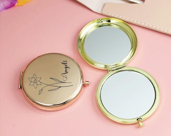 Peut inclure: Un miroir compact de couleur dorée avec un motif floral et le nom "Angeli" gravé sur le devant. Le miroir est fermé sur l'image.