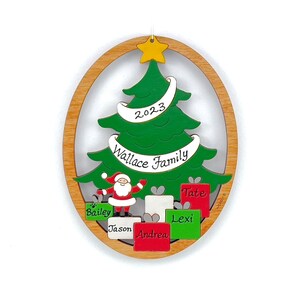 Könnte beinhalten: Ein hölzerner Weihnachtsbaum-Anhänger in Form eines Baumes mit einem weißen Banner, auf dem "2023 Wallace Family" steht. Der Weihnachtsmann steht vor dem Baum mit Geschenken, auf denen die Namen "Bailey", "Jason", "Andrea", "Lexi" und "Tate" stehen.