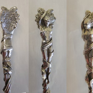Op de afbeelding: Een zilveren lepel met een gedetailleerd ontwerp van een vrouwenfiguur die in wijnstokken is gewikkeld. De steel van de lepel is gemarkeerd met het woord "Duer" en een nummer.