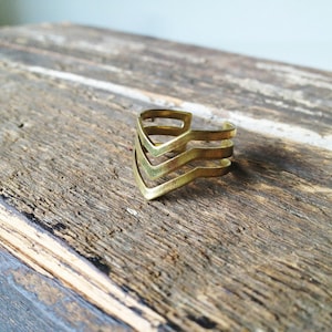 Può includere: Un braccialetto rigido in metallo dorato con un design a chevron. Il braccialetto è composto da tre strati di metallo, ognuno con un diverso motivo a chevron.