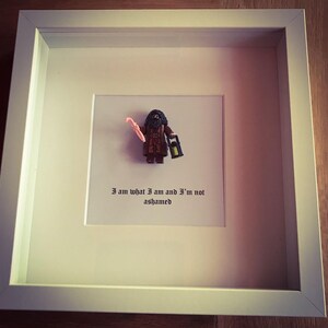 May include: A framed image of a Lego minifigure of a wizard holding a pink wand and a lantern. The text "I am what I am and I'm not ashamed" is printed below the minifigure.
