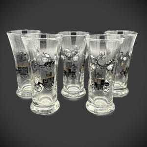 May include: Set of five clear glass tumblers with a black and gold carriage design. The glasses have a flared shape and a rounded base. The carriage design is repeated on each glass, creating a cohesive set.