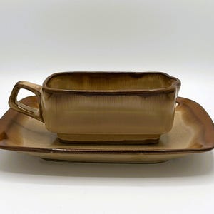 May include: A vintage ceramic cup and saucer set. The cup is rectangular with a handle, and the saucer is square with rounded corners. Both pieces have a brown and tan gradient color scheme.