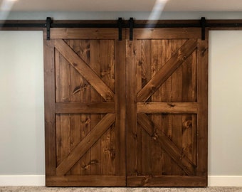 May include: A pair of brown wooden barn doors with a black metal track and hardware. The doors have a diagonal X-shaped design.