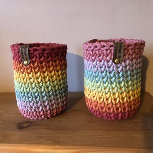 K&ouml;nnte beinhalten: Zwei handgefertigte H&auml;kel-Flaschenh&uuml;llen in einem Regenbogenverlauf. Die zylindrischen H&uuml;llen haben einen dunkelburgunderfarbenen oberen Teil und einen Regenbogen aus Farben, die in ein helles Rosa &uuml;bergehen. Jede hat ein Lederetikett mit der Aufschrift "Foliage & Flotsam".