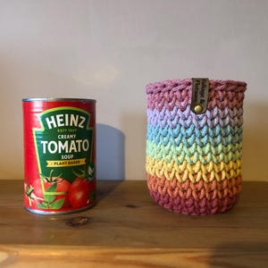 K&ouml;nnte beinhalten: Eine Dose Heinz Cremige Tomatensuppe neben einer Regenbogen-H&auml;kel-Getr&auml;nkeh&uuml;lle. Die Suppendose ist rot mit gr&uuml;nem und wei&szlig;em Text. Die H&uuml;lle ist zylindrisch, mit einem Lederetikett mit der Aufschrift "Foliage & Flotsam."