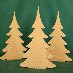 May include: Three wooden Christmas tree cutouts with a natural wood grain finish. The trees are arranged in front of a green background. Each tree has a pointed top and layered branches, creating a festive holiday decoration.