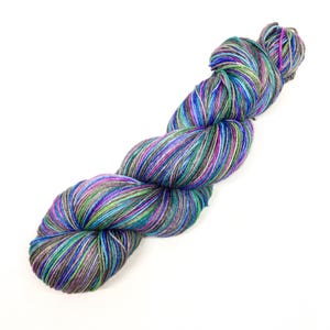 Puede incluir: Un ovillo de hilo en un patr&oacute;n jaspeado multicolor con tonos de gris, azul, verde y morado.