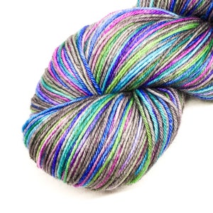 Puede incluir: Un ovillo de hilo con un patr&oacute;n de rayas multicolores en tonos de gris, azul, verde y rosa.