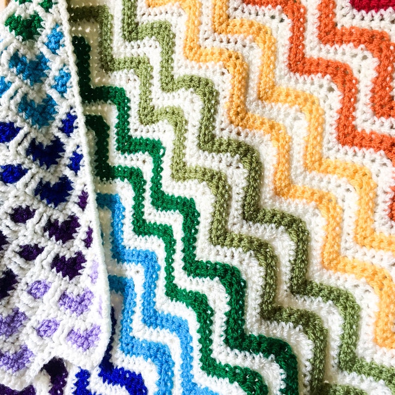 May include: A rainbow crochet blanket with a chevron pattern. The blanket is made with white yarn and different colored yarn for each stripe. The colors are purple, blue, light blue, green, yellow, orange, and red.