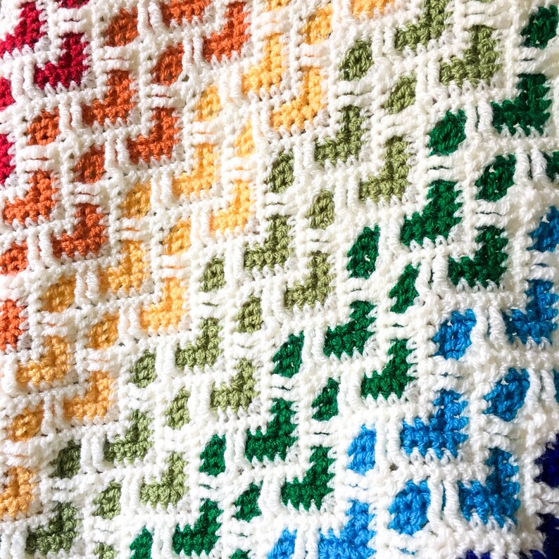 May include: A rainbow crochet blanket with a white background and a variety of colors, including red, orange, yellow, green, blue, and purple.