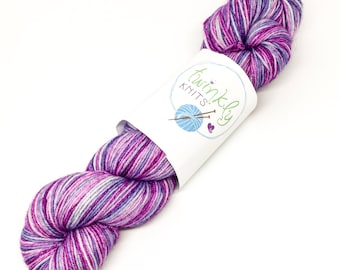 Peut inclure: Une pelote de laine violette, blanche et rose avec une étiquette blanche qui dit "Twinkly Knits".
