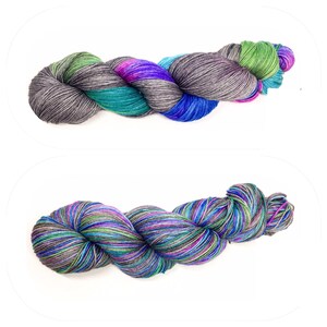 Puede incluir: Dos ovillos de hilo en un patr&oacute;n multicolor de azul, verde, morado y gris. El hilo est&aacute; dispuesto en una bobina suelta.