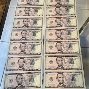 Pode incluir: Arranjo de vinte e quatro notas de cinco dólares americanos, cada uma com um retrato de Abraham Lincoln. As notas são verdes e brancas, com o texto "FIVE" e "THE UNITED STATES OF AMERICA".