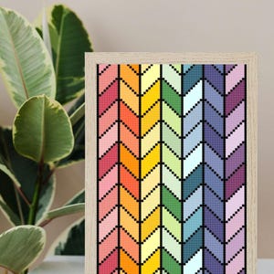 Könnte beinhalten: Ein gerahmtes Kunstwerk mit einem farbenfrohen Zickzackmuster. Das Design verwendet ein Farbspektrum, darunter Rot, Orange, Gelb, Grün, Blau und Lila. Das Kunstwerk befindet sich in einem hellen Holzrahmen.