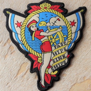 May include: A black and white embroidered patch with a sailor girl holding a ship's wheel. The background is blue and yellow with a rope design. The text "Fast Hips Sink Ships" is written on a banner.