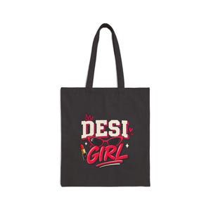 May include: A black tote bag featuring a graphic print with the text DESI GIRL in white and red lettering. The design includes a red crown, red cat-eye glasses, a red lipstick tube, and small red hearts and star accents on the front surface.