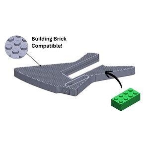 Könnte beinhalten: Eine graue Grundplatte für Bausteine mit einem kompatiblen grünen Baustein. Die Grundplatte hat eine einzigartige Form und der Text "Building Brick Compatible!" wird angezeigt.