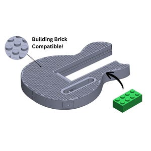 Könnte beinhalten: Eine graue, gitarrenförmige Basis für Bausteine mit strukturierter Oberfläche und einem grünen Baustein. Der Text "Building Brick Compatible!" ist ebenfalls sichtbar.