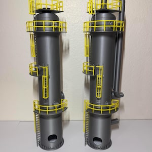 May include: Two gray industrial towers with yellow safety railings and ladders. The towers have cylindrical bodies with rounded tops and bottoms. The yellow railings and ladders provide contrast against the gray structures. The towers are likely used in chemical processing or manufacturing.