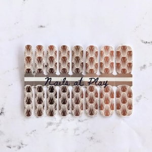 May include: A sheet of nail polish wraps with a geometric pattern in shades of brown and gold. The sheet is labeled "Nails at Play".