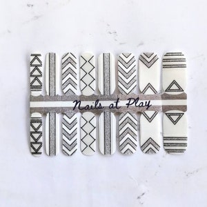 May include: A sheet of white nail polish wraps with black and silver geometric designs. The sheet is labeled "Nails at Play".