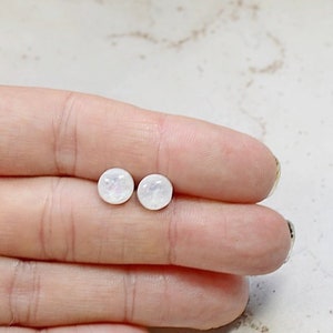 May include: A pair of small, round, white earrings with a pearlescent finish.