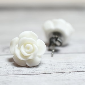 May include: A pair of white rose flower stud earrings. The earrings are made of polymer clay and have a realistic rose design.