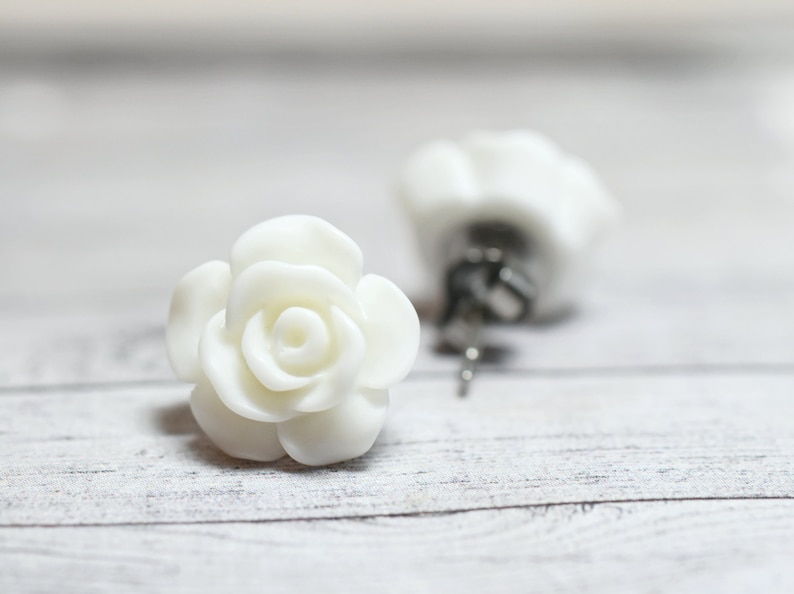 May include: A pair of white rose flower stud earrings. The earrings are made of polymer clay and have a realistic rose design.