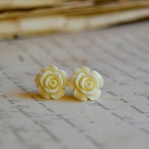 Puede incluir: Un par de pendientes de color blanco con forma de rosa. Los pendientes est&aacute;n hechos de un material liso y blanco y tienen un dise&ntilde;o delicado y femenino.