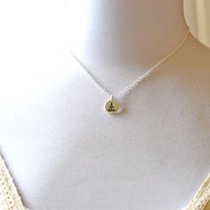 May include: A silver necklace featuring a small, round pendant with a seated Buddha figure. The pendant is attached to a delicate chain, displayed on a white mannequin. The necklace is a piece of jewelry.