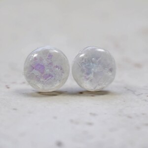 May include: A pair of white iridescent round stud earrings with a subtle sparkle.