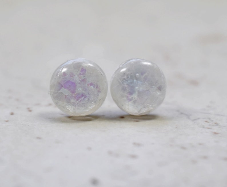 May include: A pair of white iridescent round stud earrings with a subtle sparkle.