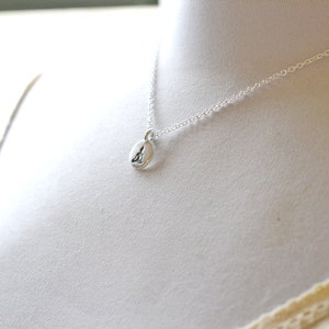 May include: A silver necklace with a small, oval pendant. The pendant features a subtle design, suspended from a delicate chain. The necklace is displayed on a white background, highlighting its simple elegance.