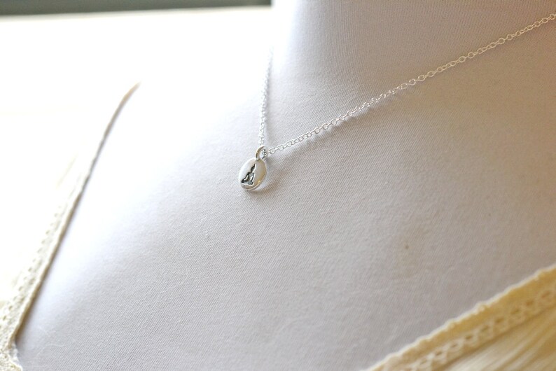 May include: A silver necklace with a small, oval pendant. The pendant features a subtle design, suspended from a delicate chain. The necklace is displayed on a white background, highlighting its simple elegance.