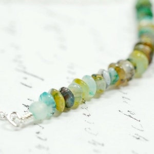 May include: A delicate necklace with a strand of green, blue, and yellow gemstone beads. The beads are round and have a natural, organic look.