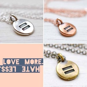 May include: Three necklaces with a round pendant featuring two parallel lines. The pendants are silver, copper, and gold. The necklaces are on a white background. The text "LOVE MORE. HATE LESS" is in the background.