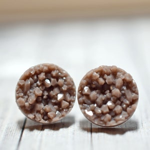 Könnte beinhalten: Ein Paar runde, braune Ohrstecker mit einer kristallartigen Textur.