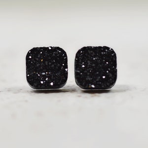 May include: A pair of black square-shaped earrings with a sparkly, textured finish.