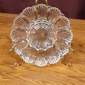 May include: A clear glass serving dish with a scalloped edge and a fluted center. The dish is on a gold metal stand.