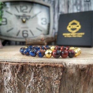May include: A beaded bracelet with blue, red, and gold beads. The bracelet is on a wooden surface.