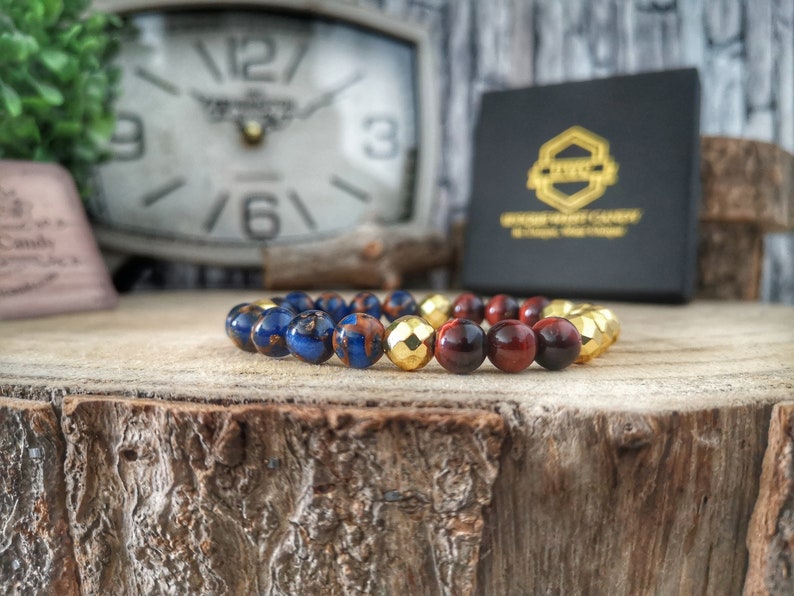 May include: A beaded bracelet with blue, red, and gold beads. The bracelet is on a wooden surface.