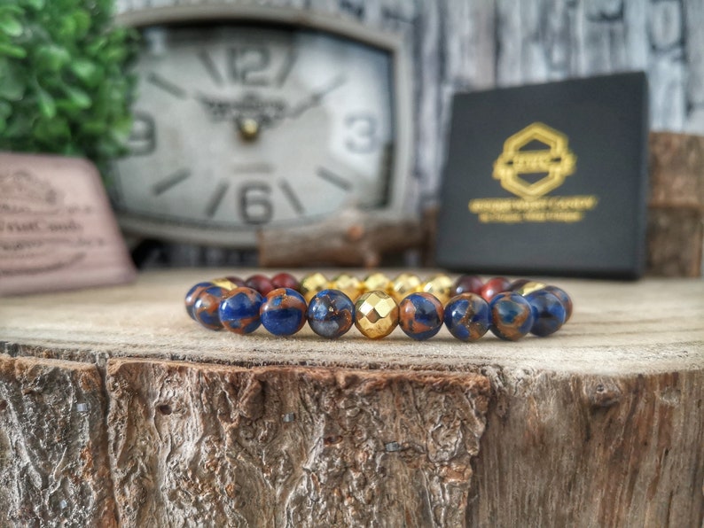 May include: A blue and brown beaded bracelet with a gold bead in the center. The bracelet is on a wooden surface.