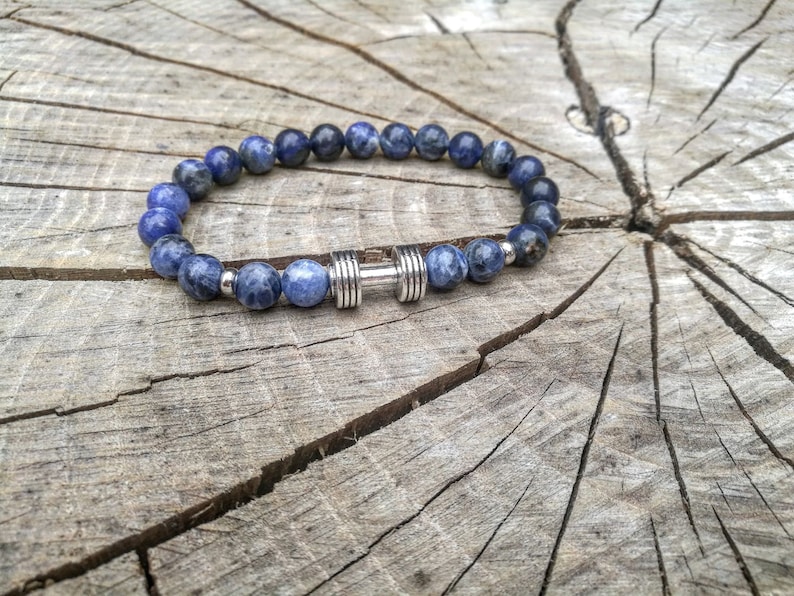 May include: A blue gemstone beaded bracelet with a silver dumbbell charm.