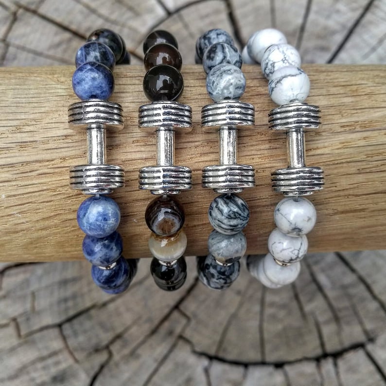 May include: Four beaded bracelets with silver dumbbell charms. The bracelets feature blue, brown, gray, and white beads.