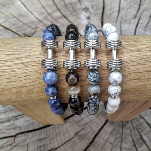 May include: Four beaded bracelets with silver dumbbell charms. The bracelets feature blue, black, gray, and white beads.