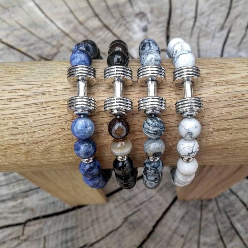 May include: Four beaded bracelets with silver dumbbell charms. The bracelets feature blue, black, gray, and white beads.