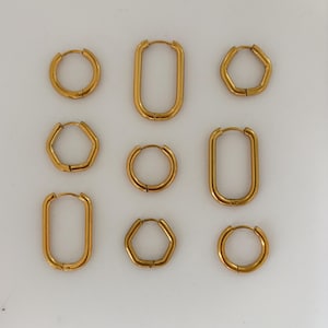 Könnte beinhalten: Neun goldfarbene Creolen in verschiedenen Formen: rund, rechteckig und fünfeckig. Die Ohrringe werden auf einer weißen Oberfläche präsentiert, die ihre polierte Oberfläche und Designvarianten hervorhebt. Eine Sammlung stilvollen Schmucks.